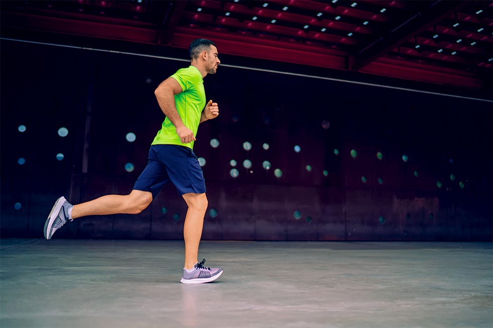 side view of strong young male jogger in activewear and sneakers running fast on empty sidewalk near wall of modern building in city