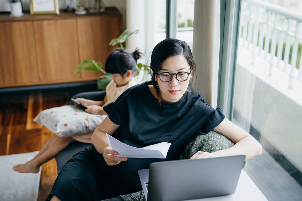 asian mother working from home on laptop while little daughter is watching on digital tablet asian family using technologies at home home office and business handling financial bills with e banking working mom managing work life and childcare at home