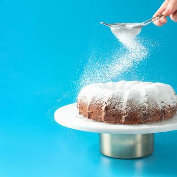 womans hand sprinkling confectioner's sugar over fresh home made bundt cake