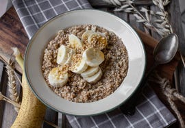 homemade fresh cooked cereal porridge with oats, amaranth and quinoa for breakfast with sliced bananas, nuts and maple syrup served on a old fahshioned enamel bowl isolatd on wooden background