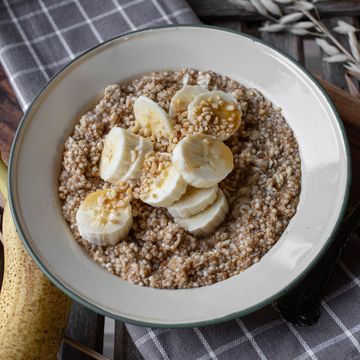 homemade fresh cooked cereal porridge with oats, amaranth and quinoa for breakfast with sliced bananas, nuts and maple syrup served on a old fahshioned enamel bowl isolatd on wooden background