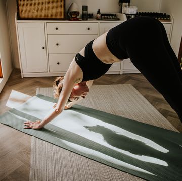 a woman enjoys some me time in a sunny room she performs a downwards dog yoga position on an exercise mat