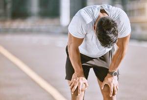 tired man resting after fitness run, taking a break from cardio training and doing wellness exercise on the road in the urban city exhausted and fit sports person doing routine workout in street