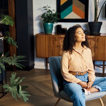 indonesian woman sitting in a room with plants with eyes closed, taking a meditation break