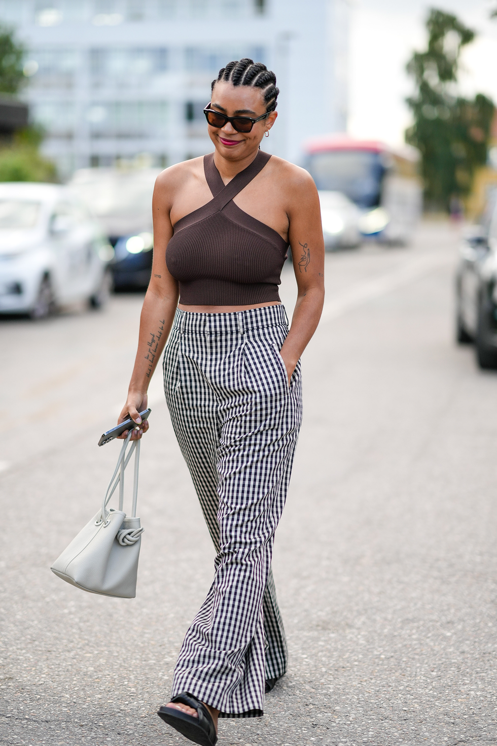 Kopenhagen, Denemarken, 9 augustus: een gast draagt ​​een zwarte zonnebril, een donkerbruine haltertop/croptop, een zwart-witte wijde broek met klein ruitjesmotief, zwarte glanzende leren sandalen met klittenbandsluiting en bandjes, een witte handtas van mat latte leer, gouden ringen, gouden oorbellen, buiten Rabens Saloner, tijdens de Copenhagen Fashion Week lente/zomer 2023, op 9 augustus 2022 in Kopenhagen, Denemarken. (foto door Edward Berthelot/Getty Images)