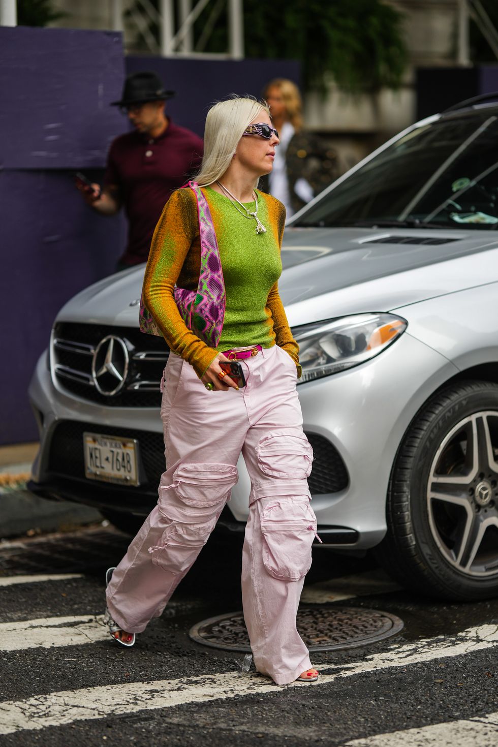 new york, new york september 12 a guest wears black and purple print pattern sunglasses from balenciaga, a green and orange gradient pattern glitter long sleeves t shirt, silver chain pendant necklaces, a pink purple green shiny leather print pattern shoulder bag, a neon pink shiny leather belt, pale pink large cargo pants, silver shiny leather nailed studded sandals from balenciaga , outside carolina herrera, during new york fashion week, on september 12, 2022 in new york city photo by edward berthelotgetty images