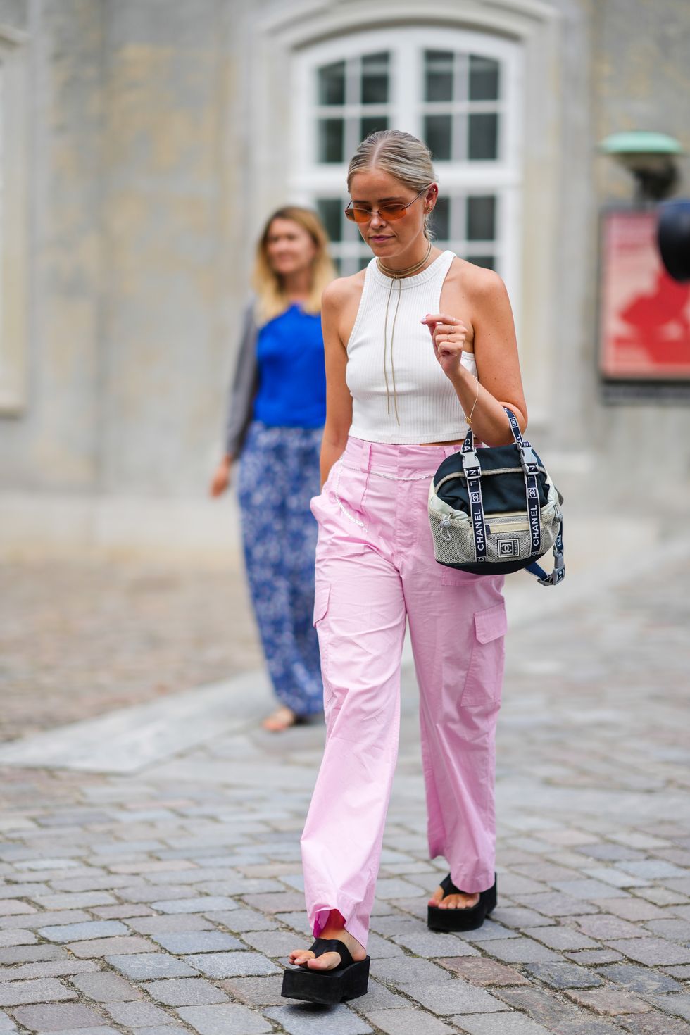copenhagen, denmark august 09 a guest wears orange sunglasses, gold and diamonds earrings, a brown suede necklace, a white ribbed halter neck cropped tank top, pale pink large cargo pants, a beige and black fabric handbag from chanel, black platform flip flop , outside aeron, during copenhagen fashion week springsummer 2023, on august 09, 2022 in copenhagen, denmark photo by edward berthelotgetty images
