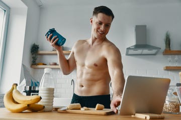 happy young man preparing protein drink and using digital tablet while standing at the kitchen