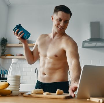 happy young man preparing protein drink and using digital tablet while standing at the kitchen