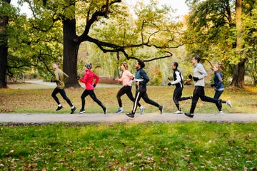 a group of joggers racing against each other on pedestrian walk way at the park.
