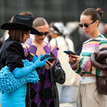 drie vrouwen op straat in kleurrijke kleding, kijkend op hun telefoon