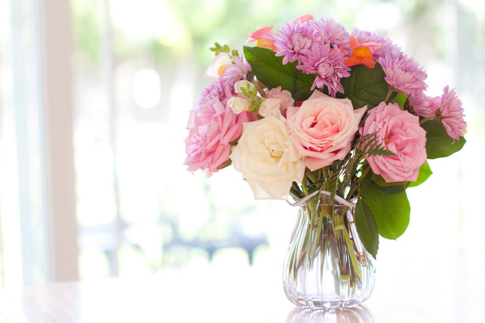 bouquet of roses, snapdragons, chrysanthemums, and greenery in pink ruffled vase on tabler in front of sunlit window