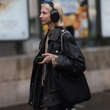 A person wearing headphones while holding a smartphone and a bag walking in an urban environment A person wearing headphones while holding a smartphone and a bag walking in an urban environment