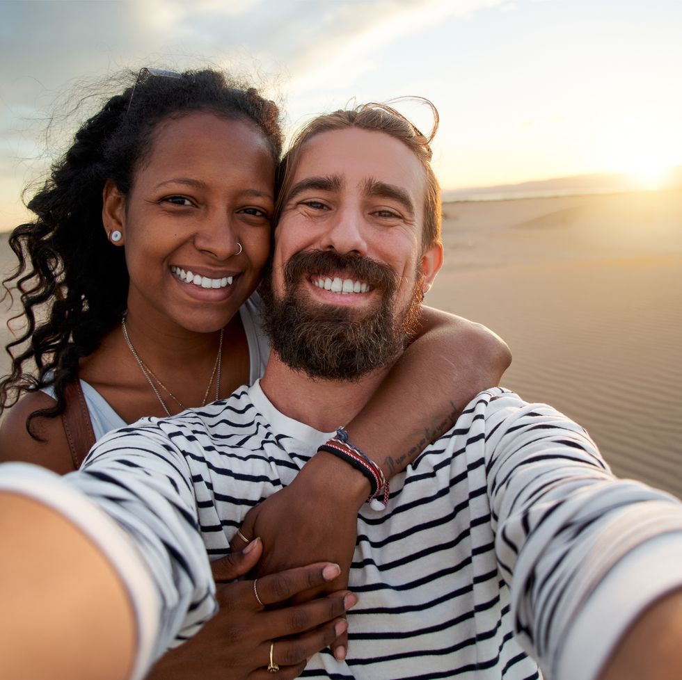 young mixed race couple taking selfie at desert, looking at camera happily