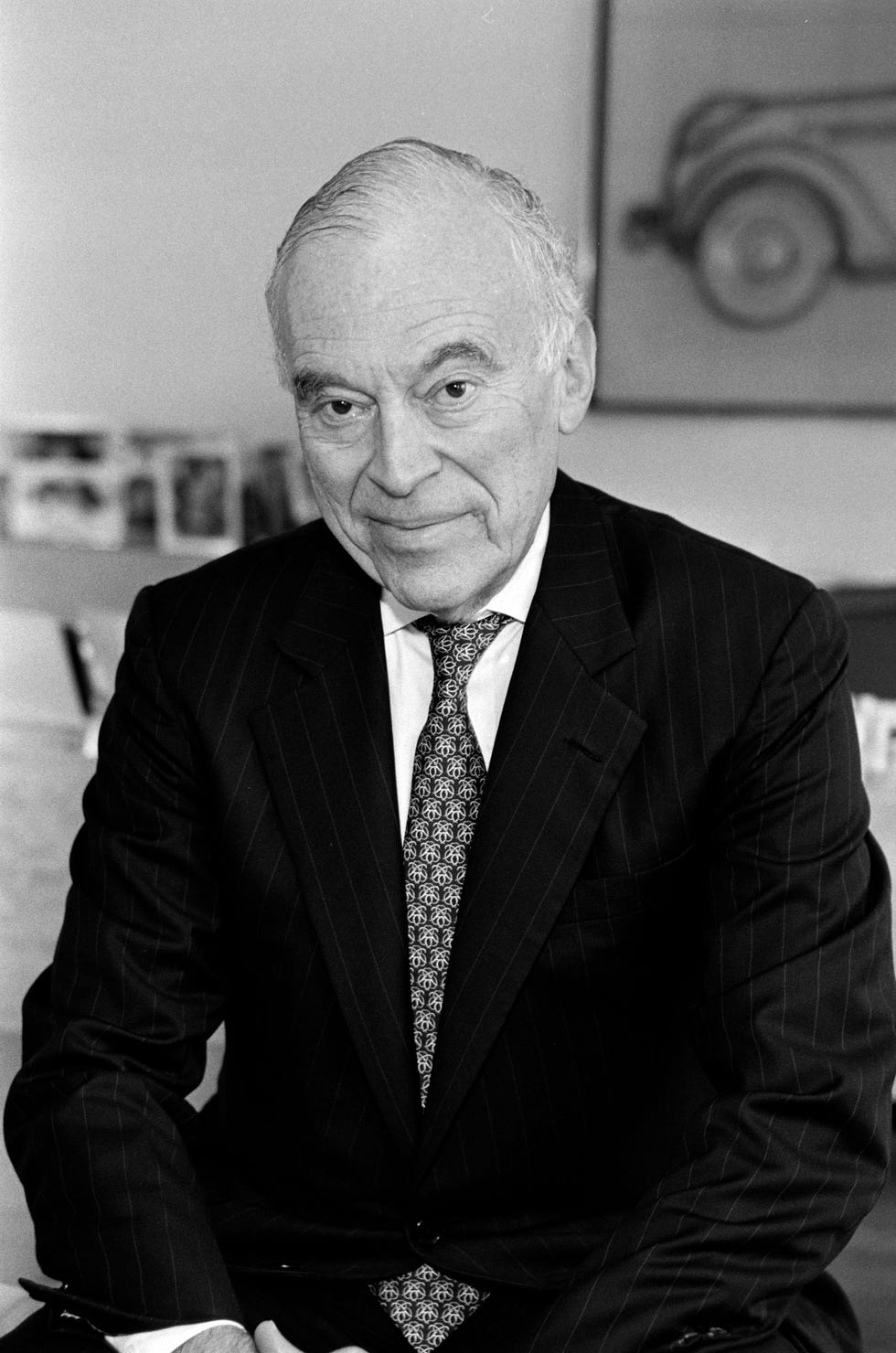 a seated individual dressed in a formal suit with a patterned tie