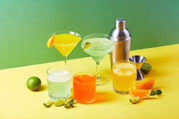 multicolored cocktails in glasses of different shapes with orange and lime on colored backgrounds with hard shadows
