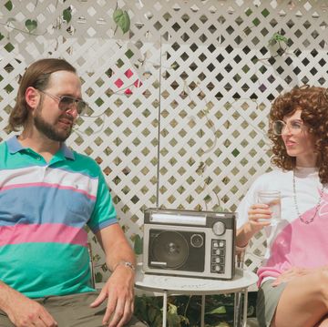 retro 1980s couple, 1980s style funny candid portrait man talking and woman listening at outdoor patio party family gathering social event man with beard is a retro man wearing eyeglasses and vintage 1980s fashion 1980s woman wearing glasses has permed hair, big curly 80s hair, and is sitting by a vintage radio man and woman having discussion where man is explaining to woman conceptual image for dating, conversation, or mansplaining