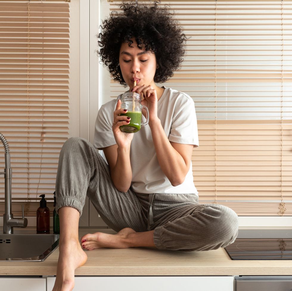 mixed race black latina woman drinking healthy green juice sitting on kitchen counter copy space healthy eating healthy lifestyle