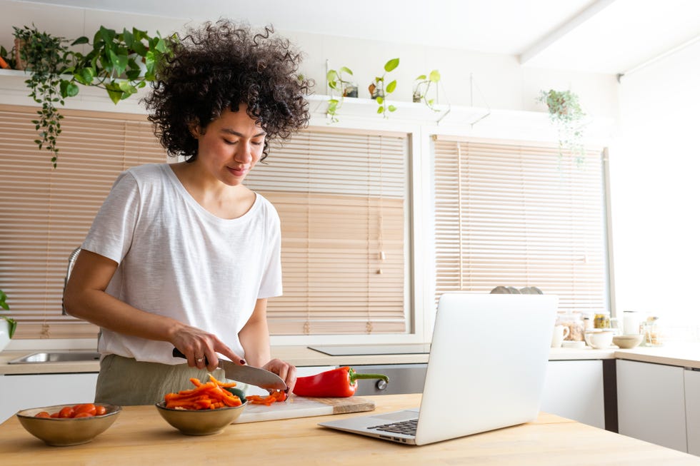 young african american woman cooking following online recipe using laptop to read ebook at home kitchen cutting peppers copy space technology concept