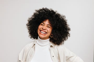 beautiful young woman with an afro hairstyle smiling at the camera while standing against a white background happy woman of color wearing her natural curly hair with pride