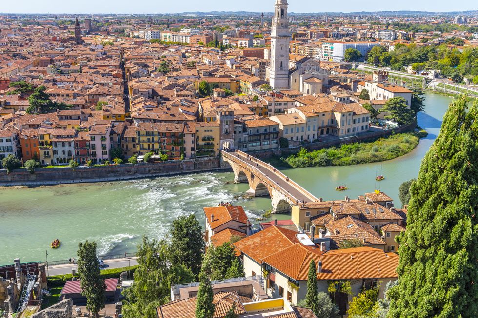 view of the historic center of the city of verona, italy and the ponte pietra bridge and river adige from the hillside fortress of castel san pietro, with groups of rafters enjoying a ride on the river