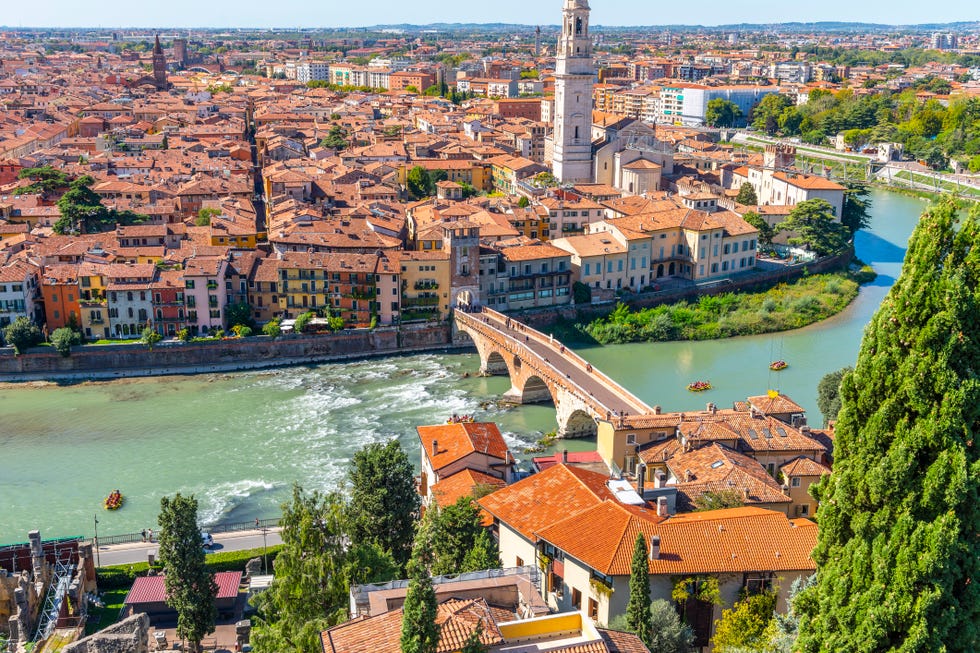 View of the historic center of the city of Verona, Italy and the Ponte Pietra bridge and river Adige from the hillside fortress of Castel San Pietro, with groups of rafters enjoying a ride on the river. view of the historic center of the city of verona, italy and the ponte pietra bridge and river adige from the hillside fortress of castel san pietro, with groups of rafters enjoying a ride on the river