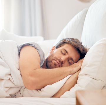 home, bedroom and sleeping man in the morning lying his head on the pillow in apartment space tired, fatigue and relax male taking time off on the weekend in bed of airbnb or hotel accommodation