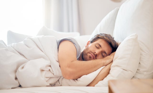 home, bedroom and sleeping man in the morning lying his head on the pillow in apartment space tired, fatigue and relax male taking time off on the weekend in bed of airbnb or hotel accommodation