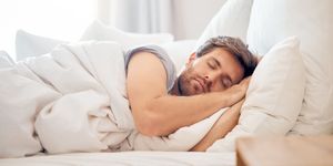 home, bedroom and sleeping man in the morning lying his head on the pillow in apartment space tired, fatigue and relax male taking time off on the weekend in bed of airbnb or hotel accommodation