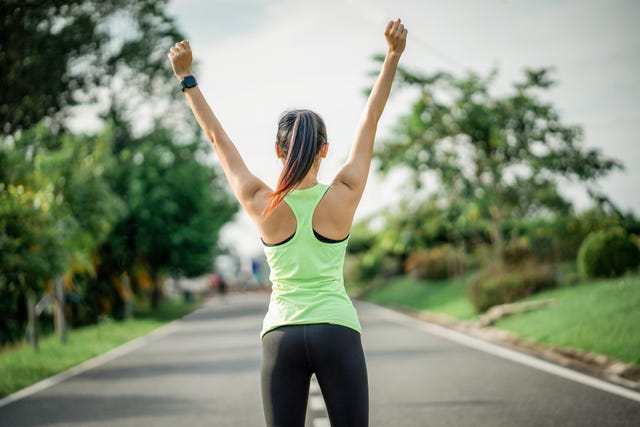 sport and life achievements and success concept fitness female athlete with arms up celebrating success and goals after sport exercising and working out young women raising hands up against sky