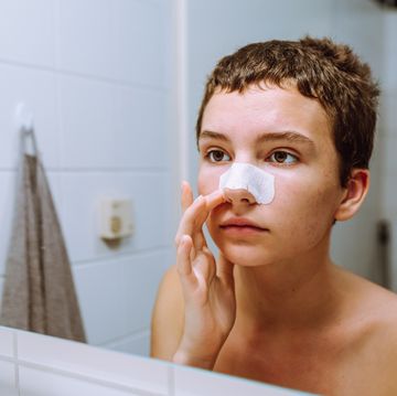 teenage girl, with short haircut, looks at reflection in mirror, on nose there is cosmetic patch for
