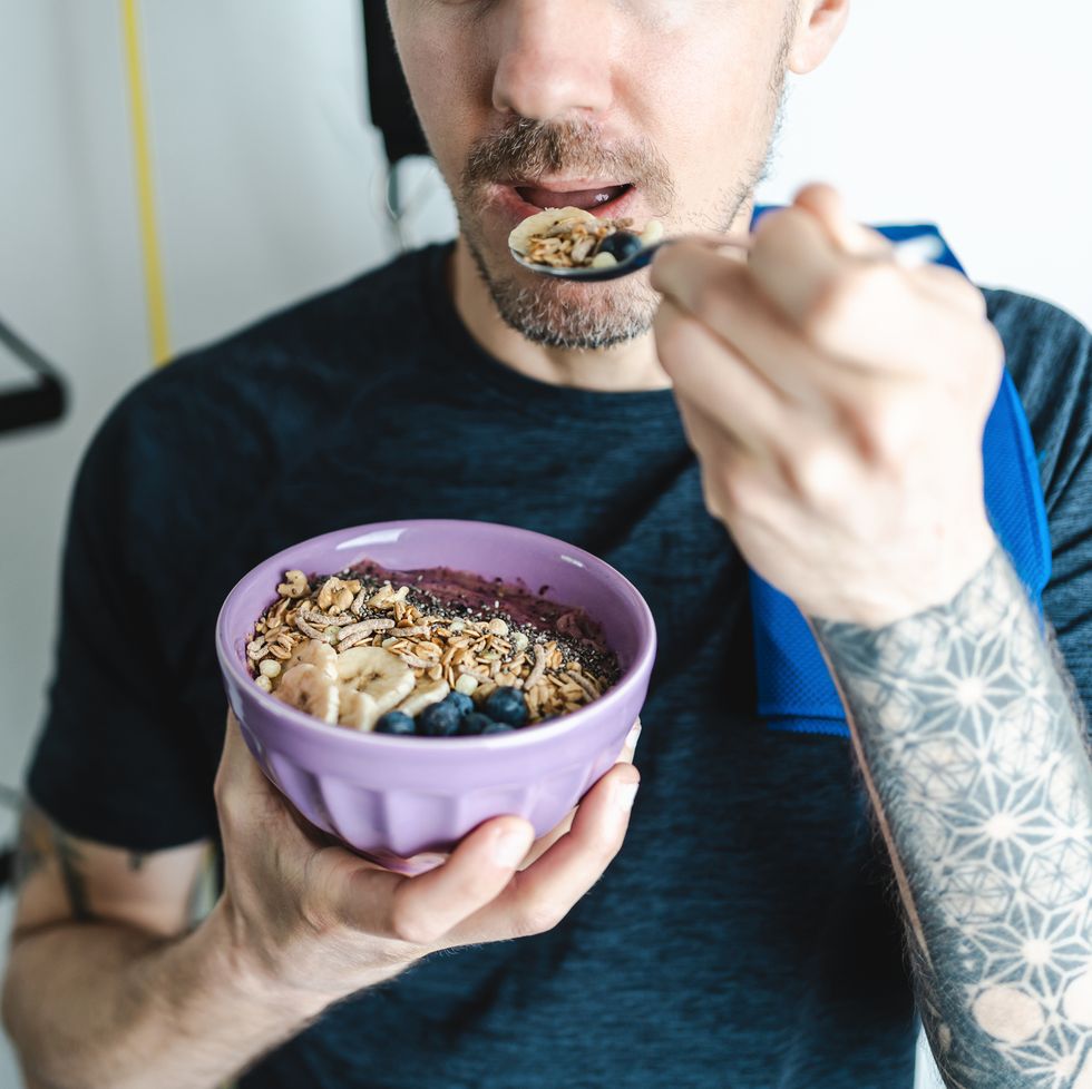 young adult man eating nutritious granola bowl after workout at home close up caption unrecognizable person