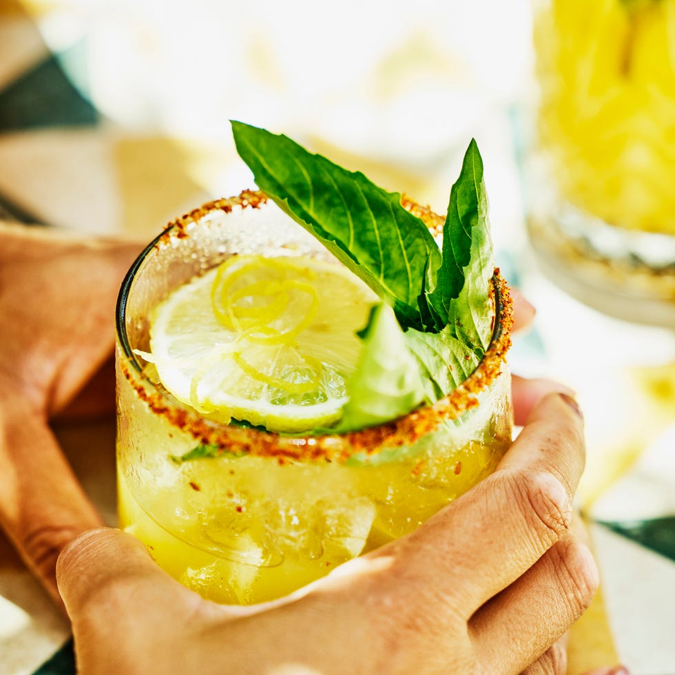 close up shot of mature womans hands holding margarita at table in tropical beach cafe