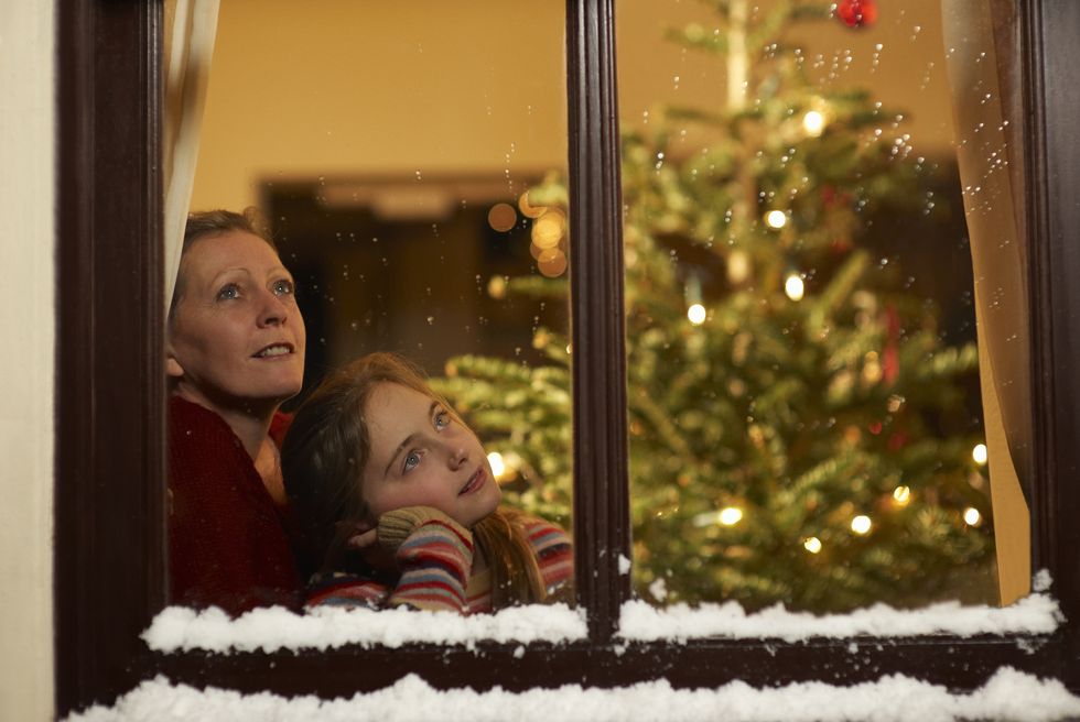 girl and mother gazing out of window at christmas