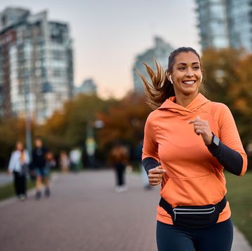 young happy athletic woman listening music on earphones while jogging in the park