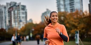 young happy athletic woman listening music on earphones while jogging in the park