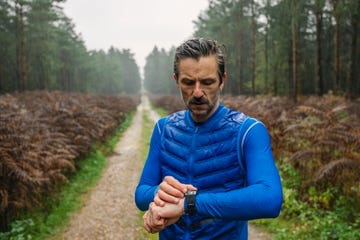 A person checking their watch while jogging on a forest path