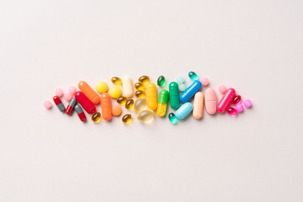 a group of multi colored medical pills organized in a row directly above view on beige background