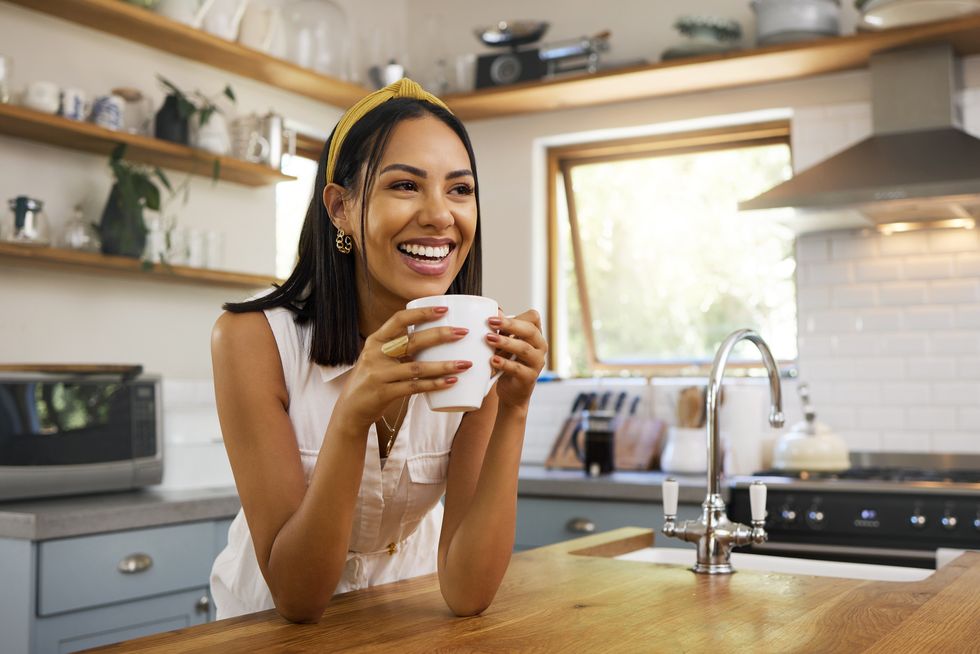 happy woman, coffee or tea in home kitchen and relax with a smile in the morning at house calm young person, smiling at peace and caffeine drink to wake up to start day with positive productive vibe
