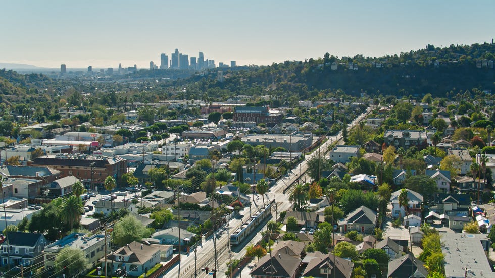 drone shot tracking a gold line train in highland park, northeast los angeles with the downtown skyline in the distance