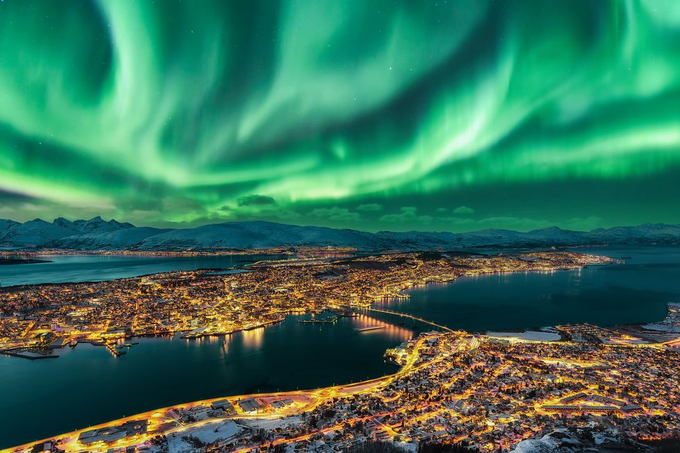 aurora borealis dancing over tromso urban skyline tromso panorama and winter night landscape with northern lights aurora polaris on a cold night, with starry sky, polar lights and snowcapped mountains on kvaloya island in the background cityscape with brightly street light of the arctic capital, northern norway