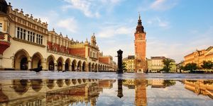 cloth hall market and the town hall tower on rynek main square in krakow old town, poland, reflecting in the rain puddle