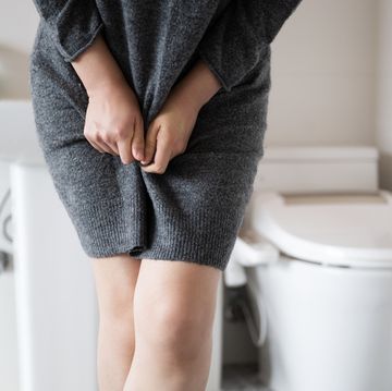 a woman wearing knitwear is complaining of pain from urinary incontinence in front of the toilet