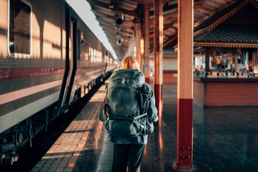 a woman stands at a train station with a backpack