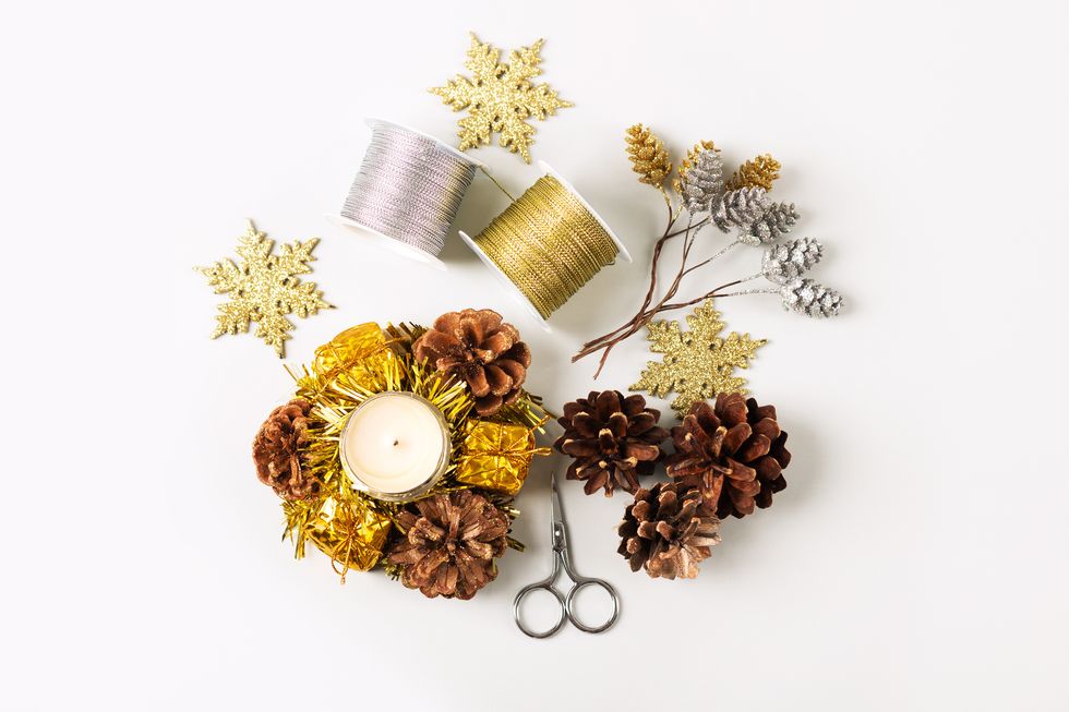 set for making for christmas decorations on the table from scissors, jewelry, ribbon, cones and candles on a beige background