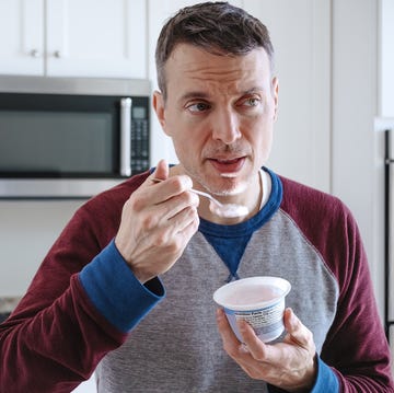 close up of mid adult white man eating a cup of yogurt while standing in kitchen