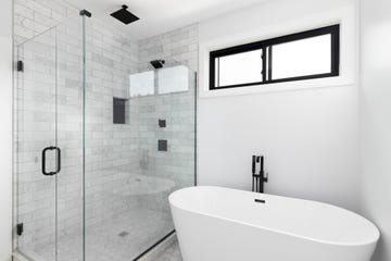 a renovated, luxury shower and freestanding bathtub with marble subway tiles, black faucet and shower head, and glass surrounding the shower