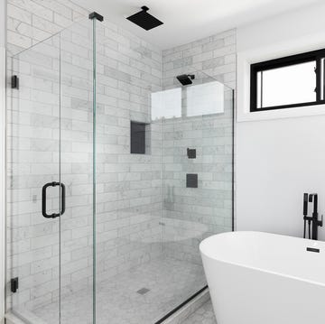 A bathroom's freestanding tub and marble tiled shower. a renovated, luxury shower and freestanding bathtub with marble subway tiles, black faucet and shower head, and glass surrounding the shower