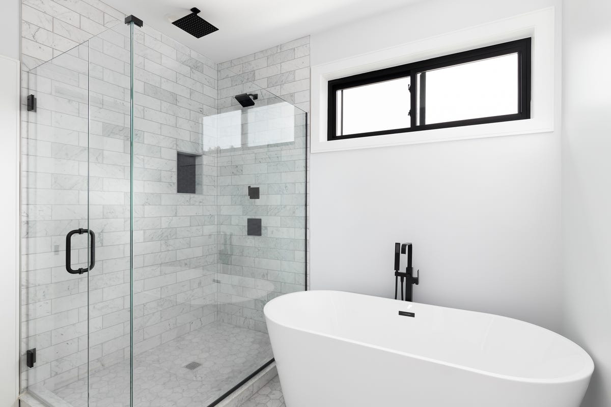 a renovated, luxury shower and freestanding bathtub with marble subway tiles, black faucet and shower head, and glass surrounding the shower
