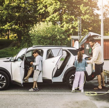 Family charging electric car at station a group of people standing next to a car that is being towed